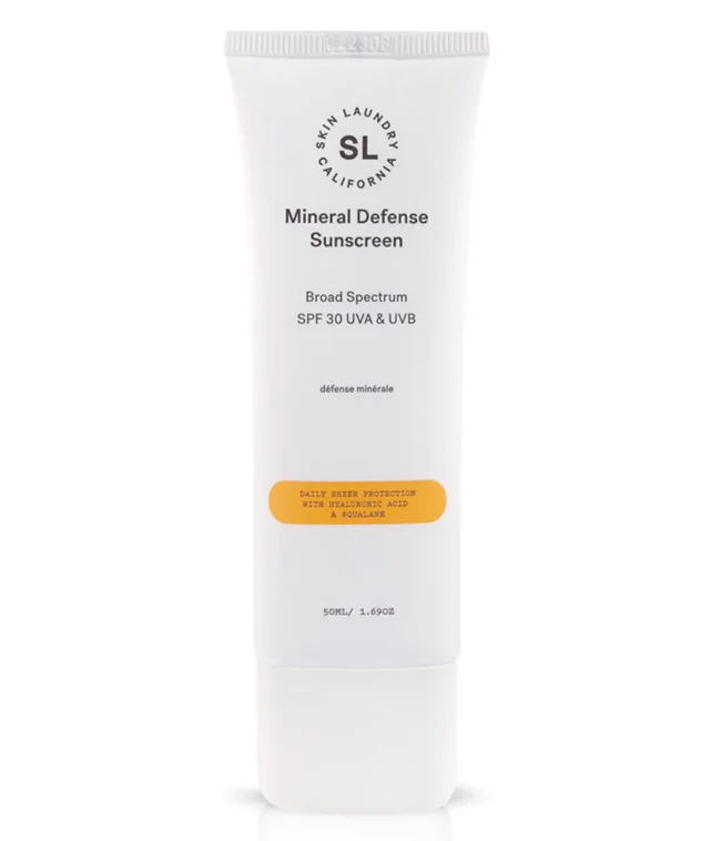 A white tube of Skin Laundry Mineral Defense Sunscreen SPF 30 UVA & UVB, standing upright with its label clearly visible, highlighting "DAILY SHEER PROTECTION WITH HYALURONIC ACID & SQUALANE."