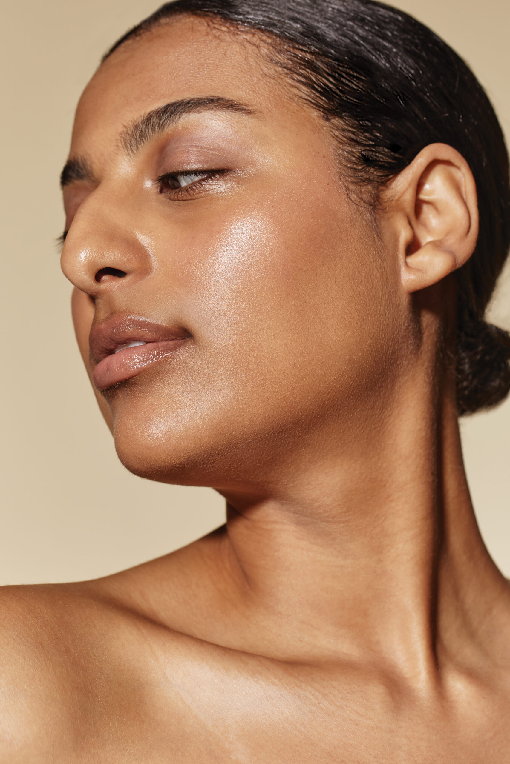 A close-up profile shot of a person with clear, glowing skin and dark hair pulled back, looking subtly downwards, highlighting a radiant and healthy complexion.