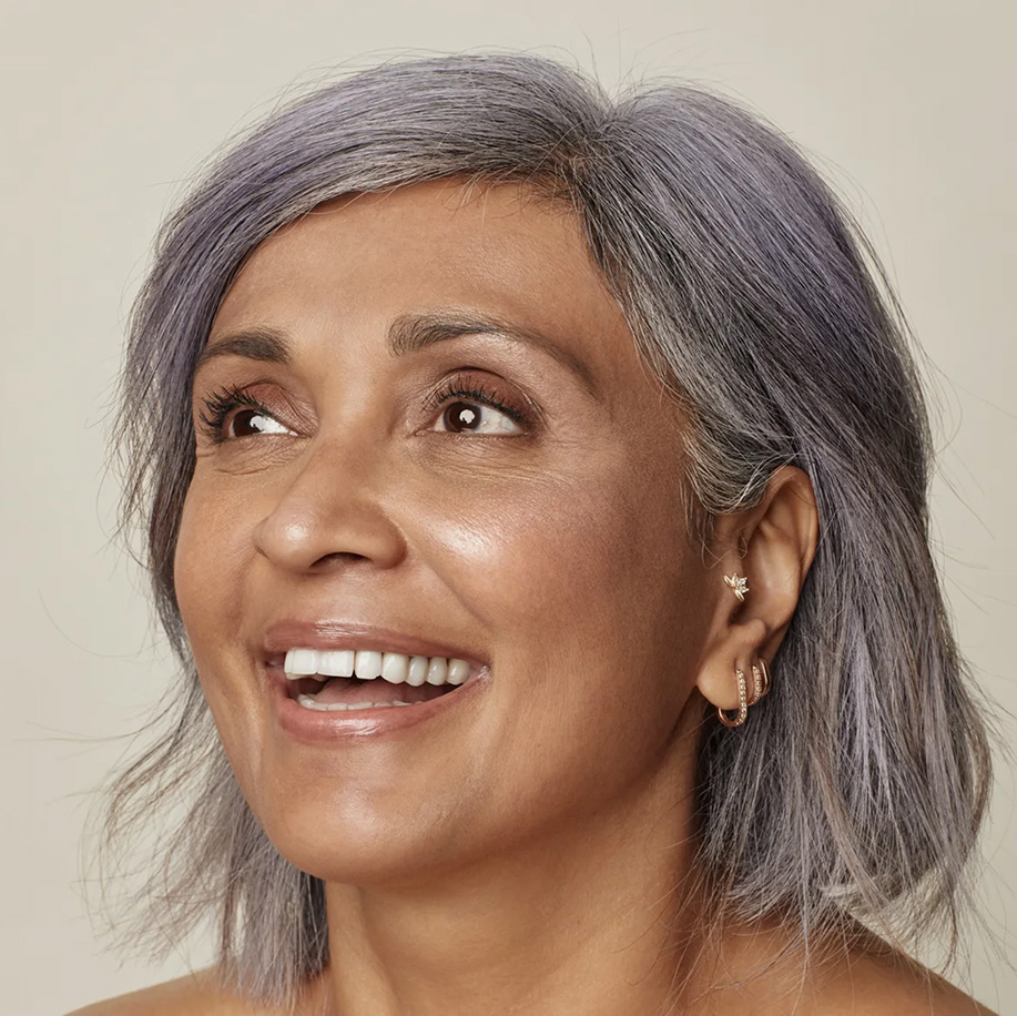 Smiling person with radiant, healthy skin and stylish short grey hair, wearing hoop and star-shaped earrings. Showcases natural glow and confidence.